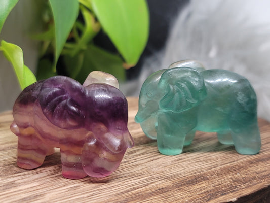 Two fluorite cared elephants on a wood plank.